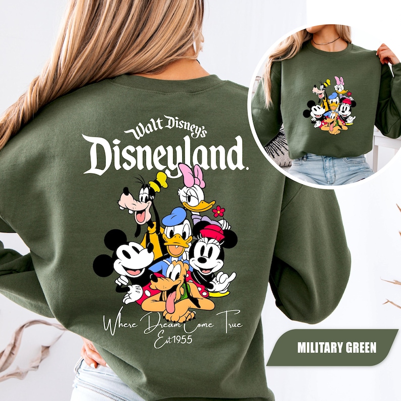 May include: A military green crewneck sweatshirt featuring a large graphic on the back with the text Walt Disney's Disneyland Where Dreams Come True Est 1955 and a group of cartoon characters including Mickey, Minnie, Donald, Daisy, Goofy, and Pluto.