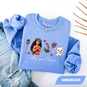 Pu&ograve; includere: Felpa blu Carolina con una grafica di una donna, un gallo, un maiale e altri elementi. Il testo "How far I'll go" &egrave; stampato sotto la grafica. La felpa &egrave; realizzata in materiale morbido e ha maniche lunghe.