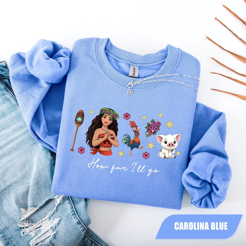 Pu&ograve; includere: Felpa blu Carolina con una grafica di una donna, un gallo, un maiale e altri elementi. Il testo "How far I'll go" &egrave; stampato sotto la grafica. La felpa &egrave; realizzata in materiale morbido e ha maniche lunghe.