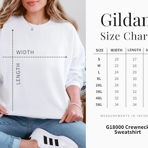 Puede incluir: Una sudadera Gildan blanca con cuello redondo y una tabla de tallas. La tabla muestra las medidas en pulgadas de ancho, largo y largo de manga, desde la talla S hasta la 5XL. La sudadera es G18000.