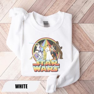 May include: White sweatshirt featuring a colorful Star Wars graphic with characters and the Star Wars logo. The graphic is set against a rainbow background. The word "WHITE" is displayed at the bottom.