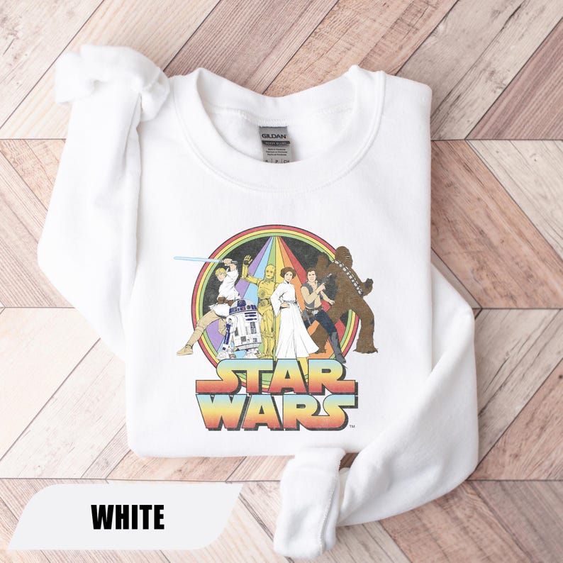 May include: White sweatshirt featuring a colorful Star Wars graphic with characters and the Star Wars logo. The graphic is set against a rainbow background. The word "WHITE" is displayed at the bottom.