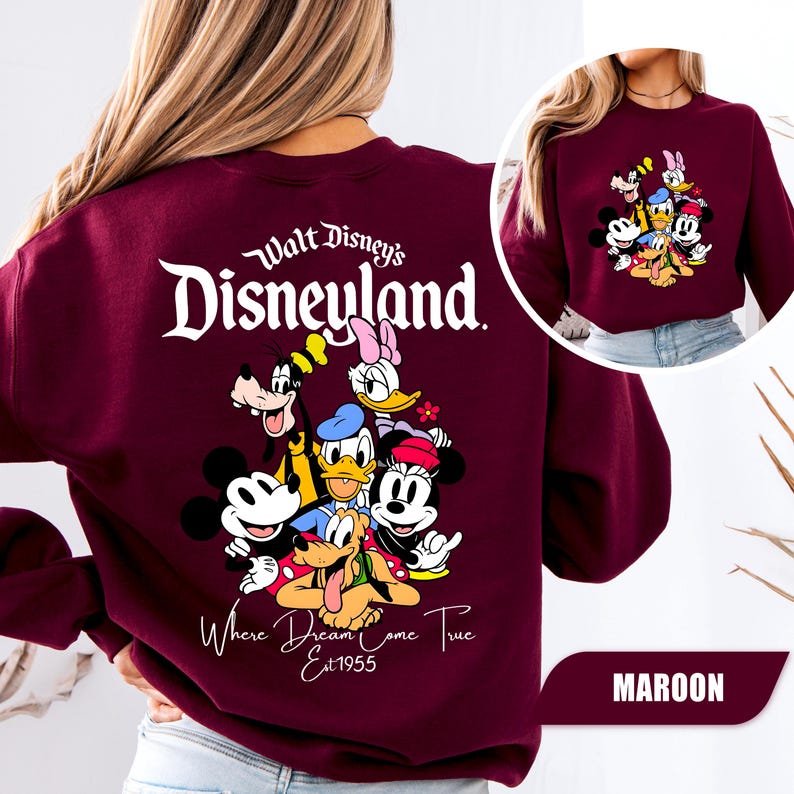 May include: A maroon long-sleeve sweatshirt featuring a large graphic on the back with the text Walt Disney's Disneyland Where Dreams Come True Est 1955 and illustrations of Mickey Mouse, Minnie Mouse, Donald Duck, Daisy Duck, Goofy, and Pluto.