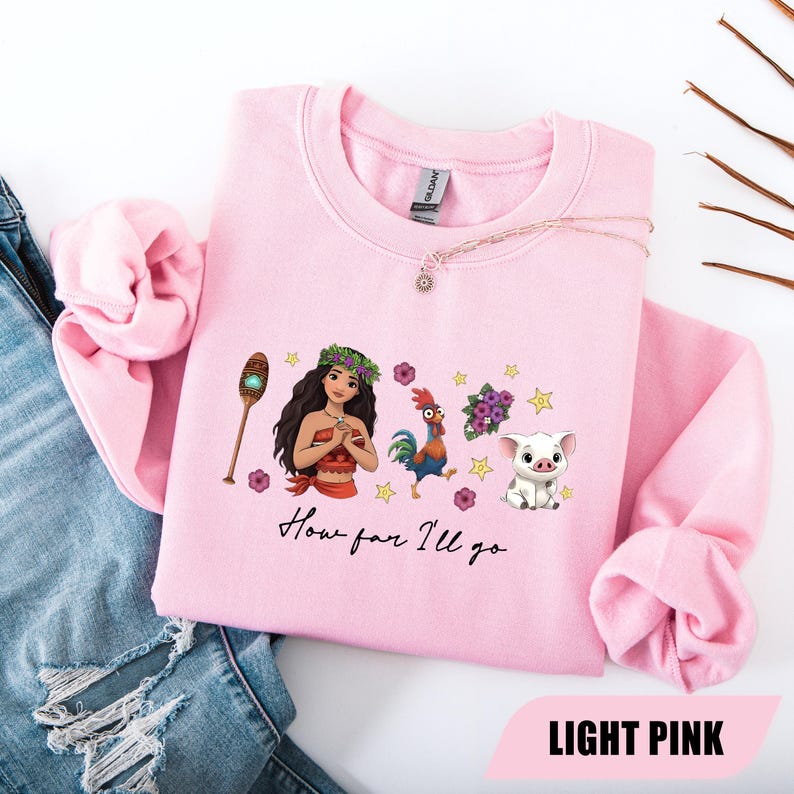 Pu&ograve; includere: Felpa rosa chiaro con una grafica di una donna polinesiana, un gallo, un maiale e la scritta "How far I'll go". Il design include elementi floreali e stelle. La parte inferiore della felpa riporta la scritta "LIGHT PINK".