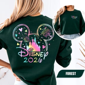 Puede incluir: Sudadera verde bosque con un dise&ntilde;o colorido de Disney 2026 en la espalda, que incluye un castillo, fuegos artificiales y orejas de Mickey Mouse. La parte delantera de la sudadera tiene un dise&ntilde;o m&aacute;s peque&ntilde;o de Disney 2026. La palabra "FOREST" est&aacute; en la parte inferior.