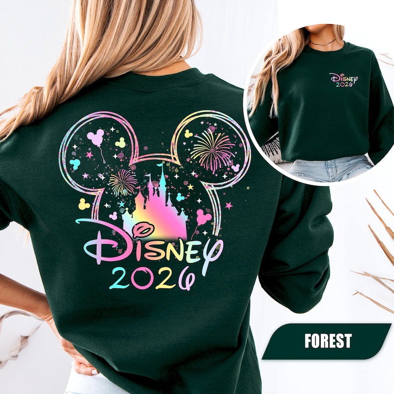 Puede incluir: Sudadera verde bosque con un dise&ntilde;o colorido de Disney 2026 en la espalda, que incluye un castillo, fuegos artificiales y orejas de Mickey Mouse. La parte delantera de la sudadera tiene un dise&ntilde;o m&aacute;s peque&ntilde;o de Disney 2026. La palabra "FOREST" est&aacute; en la parte inferior.
