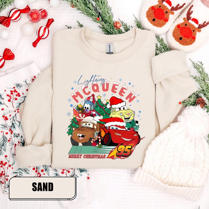 May include: Sand-colored sweatshirt featuring a graphic of Lightning McQueen and other Cars characters wearing Santa hats, with the text "Lightning McQueen" and "Merry Christmas". The number "95" is also visible.