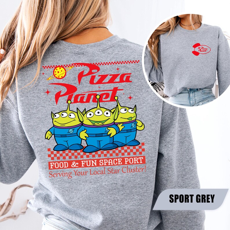 Puede incluir: Sudadera gris deportivo con el logo de Pizza Planet y tres personajes alien&iacute;genas verdes. El dise&ntilde;o trasero incluye las palabras "Pizza Planet" en rojo, con la frase "FOOD & FUN SPACE PORT Serving Your Local Star Cluster!"