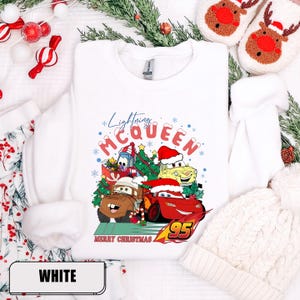 May include: White crewneck sweatshirt featuring a colorful graphic of Lightning McQueen and other Cars characters wearing Santa hats, with the text "Lightning McQueen" and "Merry Christmas".