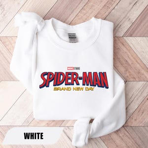 Puede incluir: Sudadera blanca con el logo de Spider-Man en rojo y azul, con detalles amarillos. El texto "BRAND NEW DAY" est&aacute; debajo del logo. El logo de Marvel Studios est&aacute; encima del texto de Spider-Man. La palabra "WHITE" est&aacute; en la parte inferior.