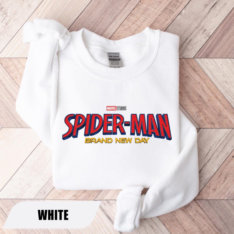 Puede incluir: Sudadera blanca con el logo de Spider-Man en rojo y azul, con detalles amarillos. El texto "BRAND NEW DAY" est&aacute; debajo del logo. El logo de Marvel Studios est&aacute; encima del texto de Spider-Man. La palabra "WHITE" est&aacute; en la parte inferior.