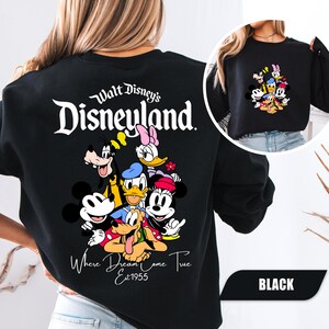 May include: A black crewneck sweatshirt featuring a large graphic on the back with the text Walt Disney's Disneyland Where Dreams Come True Est 1955 and a group of cartoon characters including Mickey, Minnie, Donald, Daisy, Goofy, and Pluto.