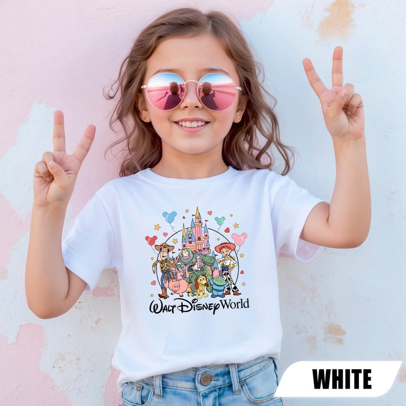 Puede incluir: Una camiseta blanca con un gr&aacute;fico colorido de personajes de Disney y un castillo, con el texto "Walt Disney World" en escritura negra. La camiseta la lleva una persona que lleva gafas de sol y hace el signo de la paz.