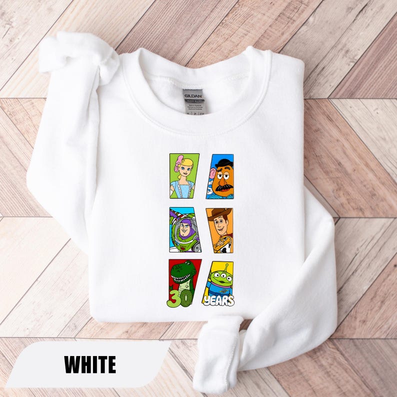 May include: A white crewneck sweatshirt featuring a graphic print of six Toy Story characters arranged in rectangular frames. The design includes Bo Peep, Mr. Potato Head, Buzz Lightyear, Woody, Rex, and an alien, with the text 30 YEARS.