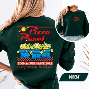 Puede incluir: Sudadera verde bosque con el logo de Pizza Planet y tres personajes alien&iacute;genas verdes con monos azules. La parte trasera de la sudadera tiene las palabras "Pizza Planet" en rojo, con la frase "Food & Fun Space Port" debajo.