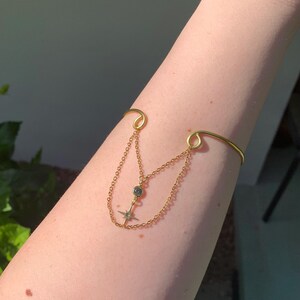 May include: A gold chain bracelet with a dangling star charm and a small round stone. The bracelet is worn on a person's arm.