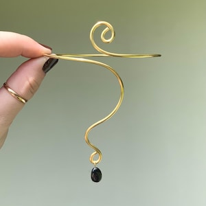 May include: Gold wire arm cuff with a black gemstone dangling from the bottom.