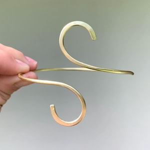 May include: A gold-toned metal bracelet with a double-loop design. The bracelet is made of a single piece of wire that is bent into two loops.