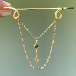 May include: A gold chain necklace with a green gemstone pendant and a star charm. The necklace is attached to a gold bar with two loops at the ends.