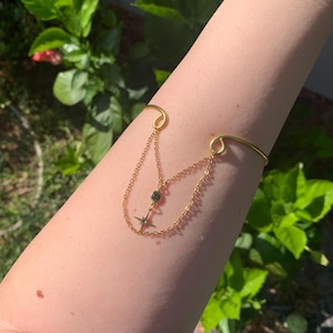 May include: A gold arm cuff with a dangling chain and a star charm. The chain has a small black gemstone.