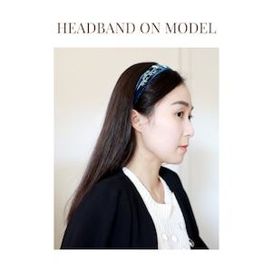 May include: A woman is wearing a blue velvet headband with a floral design. The headband is on her forehead and her hair is pulled back.