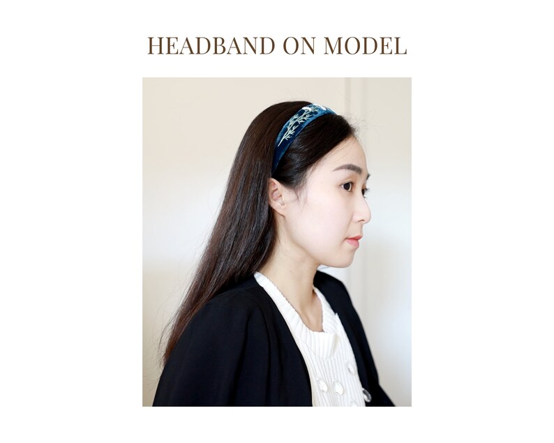 May include: A woman is wearing a blue velvet headband with a floral design. The headband is on her forehead and her hair is pulled back.
