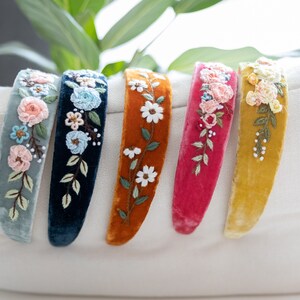 May include: Five velvet headbands with embroidered floral designs. The headbands are in shades of blue, green, orange, pink, and yellow.