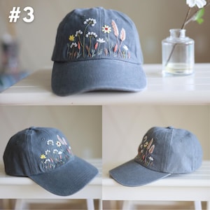 Peut inclure: Une casquette de baseball grise avec des fleurs brod&eacute;es dans des tons de rose, jaune et blanc. La casquette a une visi&egrave;re incurv&eacute;e et une sangle &agrave; l'arri&egrave;re.