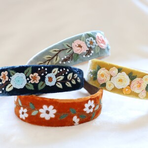 May include: Four velvet headbands with embroidered floral designs. The headbands are in shades of blue, yellow, and orange.