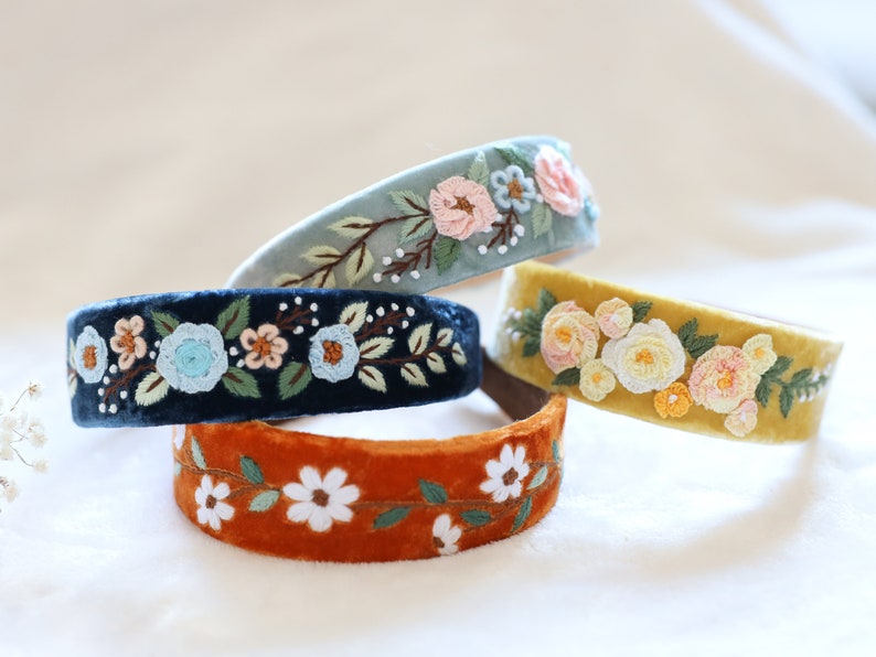 May include: Four velvet headbands with embroidered floral designs. The headbands are in shades of blue, yellow, and orange.