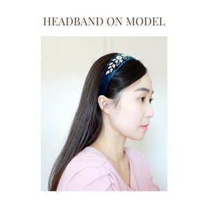 May include: A dark blue velvet headband with a gold and clear rhinestone embellishment. The headband is worn by a model with long dark hair.