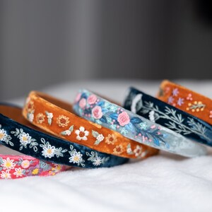 May include: Five velvet headbands with embroidered floral designs. The headbands are in shades of blue, orange, and pink.