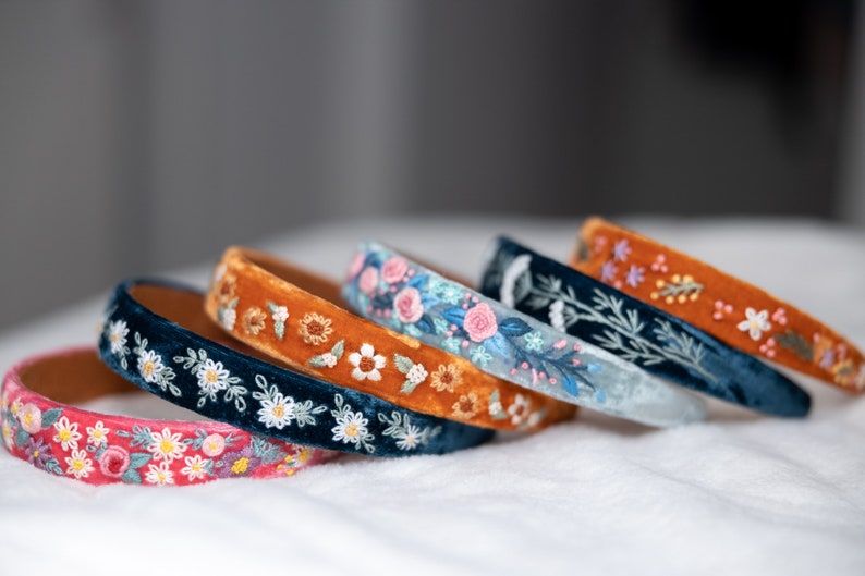 May include: Five velvet headbands with embroidered floral designs. The headbands are in shades of blue, orange, and pink.