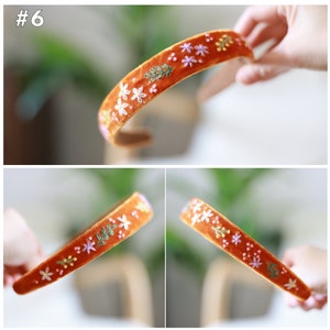 May include: A brown velvet headband with embroidered flowers and leaves in shades of pink, green, and yellow.