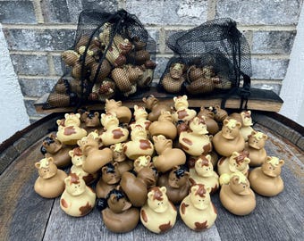 May include: A large group of brown and white rubber duckies with a horse head design. The duckies are arranged in a pile on a wooden barrel. Some of the duckies are in black mesh bags.
