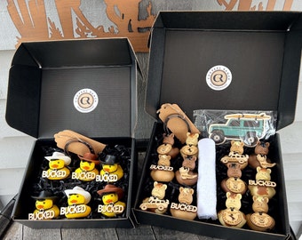 May include: Two black boxes filled with rubber duckies. The duckies are decorated with cowboy hats and western themed designs. The boxes are labeled "Cooper's Ranch".