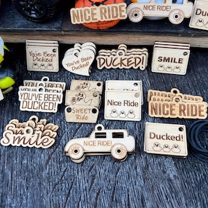 May include: A collection of wooden tags with various sayings, including "Nice Ride", "Ducked!" and "Smile". Some tags feature rubber duck illustrations.