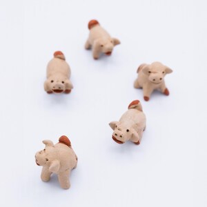 May include: Five small ceramic pig figurines in various poses, all with brown and white paint, on a white background.