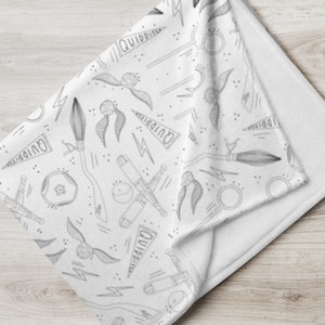 Könnte beinhalten: Eine weiße Fleece-Decke mit einem schwarz-weißen Muster aus verschiedenen Harry-Potter-Motiven, darunter ein Schnatz, ein Besen, ein Quidditch-Schläger und die Worte "Quidditch".
