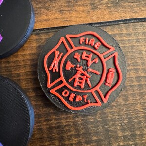 May include: Black, round coaster with a red fire department emblem. The emblem features the words "FIRE DEPT." and Chinese characters. The coaster is made of a solid material and is likely for use in a home or office setting.
