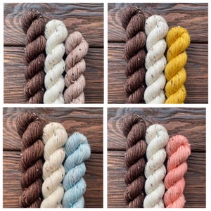 Könnte beinhalten: Vier Garnknäuel-Sets in verschiedenen Farbkombinationen. Jedes Set enthält drei Knäuel, mit Farben von Braun, Creme und Beige bis hin zu Gelb, Blau und Koralle. Das Garn hat eine gesprenkelte Textur, vor einem Holzgrund.