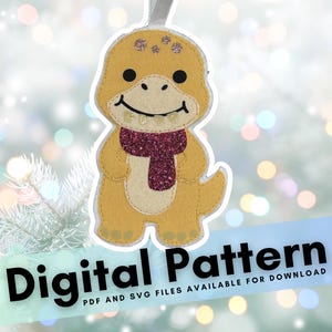 May include: A felt dinosaur ornament with a maroon glitter scarf and a smiling face. The ornament is yellow with a cream-colored belly and small glitter accents. The text "Digital Pattern" is displayed at the bottom.
