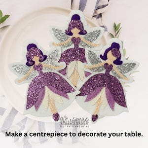 Pu&ograve; includere: Tre ornamenti di fata con glitter viola, ali bianche e sfondo bianco. Le fate indossano abiti viola e hanno i capelli viola.