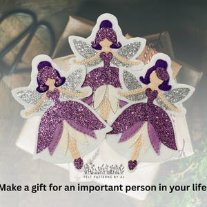 Pu&ograve; includere: Tre ornamenti di fata in feltro viola con ali di glitter argentate e dettagli bianchi. Le fate indossano abiti viola e hanno i capelli viola. Il testo "FELT PATTERNS BY AJ" &egrave; nella parte inferiore dell'immagine.