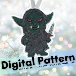 May include: Felt ornament of a green goblin with a gray hooded cloak, holding a silver and red dagger. The goblin has glittery red eyes and two large teeth. The ornament has a white ribbon for hanging. Text at the bottom reads "Digital Pattern".