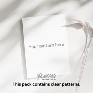 Pu&ograve; includere: Un cartoncino bianco con il testo "Your pattern here" e il logo "Felt Patterns by AJ" in basso. Il cartoncino &egrave; su una superficie bianca con steli d'erba secca e ombre.