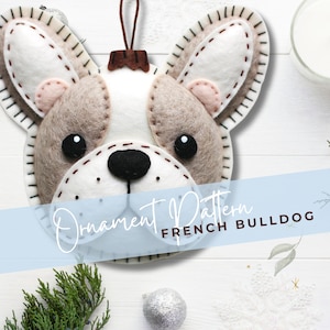 Może przedstawiać: Wz&oacute;r ozdoby filcowej dla buldoga francuskiego. Wz&oacute;r zawiera głowę psa z filcu w kolorze białym i brązowym z czarnymi oczami i nosem.