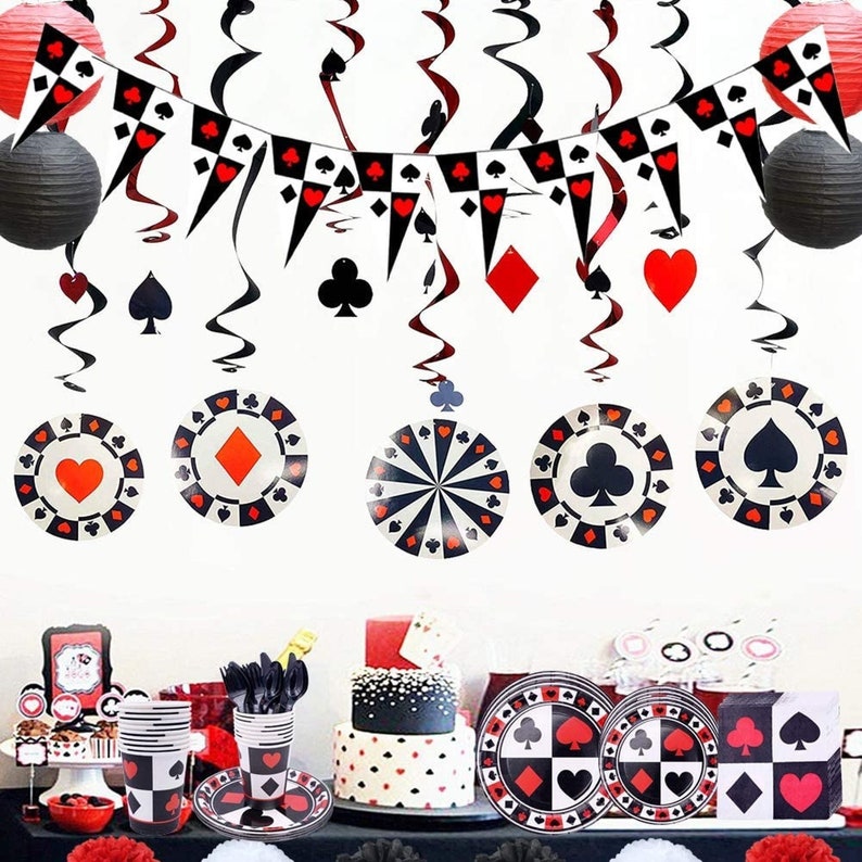 May include: A black, red and white casino themed party decoration set. The set includes a banner, hanging swirls and paper plates. The banner has red hearts, black spades and diamond symbols. The hanging swirls have a black and white chequered pattern. The paper plates have a black and white chequered pattern with red hearts, black spades and diamond symbols.