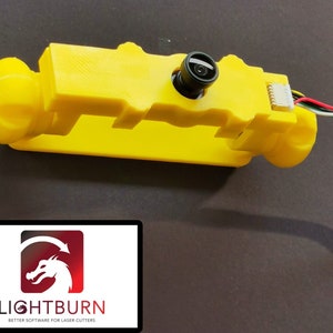 May include: A yellow 3D printed camera mount with a black camera lens and a cable attached. The mount has a threaded hole on the side. The camera is mounted on a black surface.