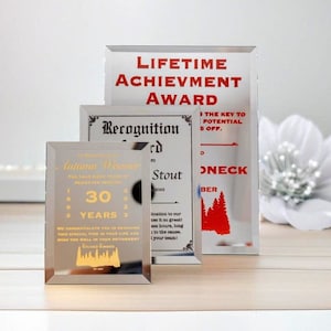 Puede incluir: Tres premios de vidrio con texto. El m&aacute;s grande dice "LIFETIME ACHIEVEMENT AWARD" en rojo. El premio del medio dice "Recognition Award" y el m&aacute;s peque&ntilde;o dice "30 YEARS" con el nombre "Autumn Weaver".